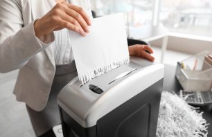 Close-up of a person feeding a white sheet of paper into an office paper shredder, ensuring the secure destruction of confidential documents and protecting sensitive information.