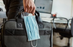 closeup of a young man in an office holding a briefcase and a surgical mask in his hand