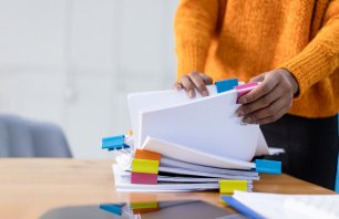 African American woman working with paper documents and stacks packs pile on the desk in the office.